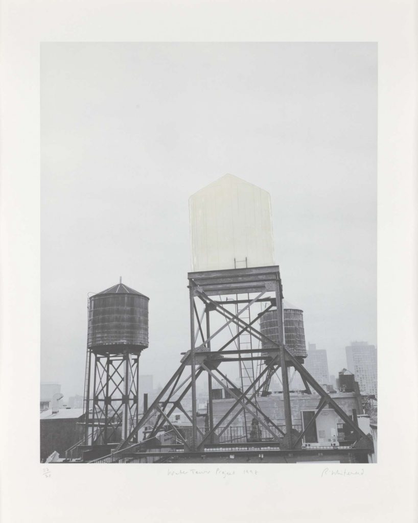 A black-and-white photograph of rooftops showing a ghostly white water tower among two other regular ones