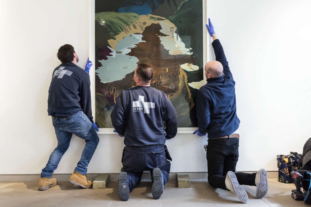 3 art technicians installing a large painting on a wall