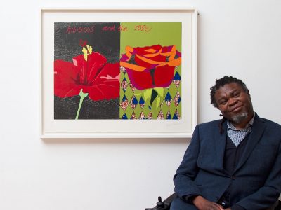 an artist sitting down with his work of art on the wall behind