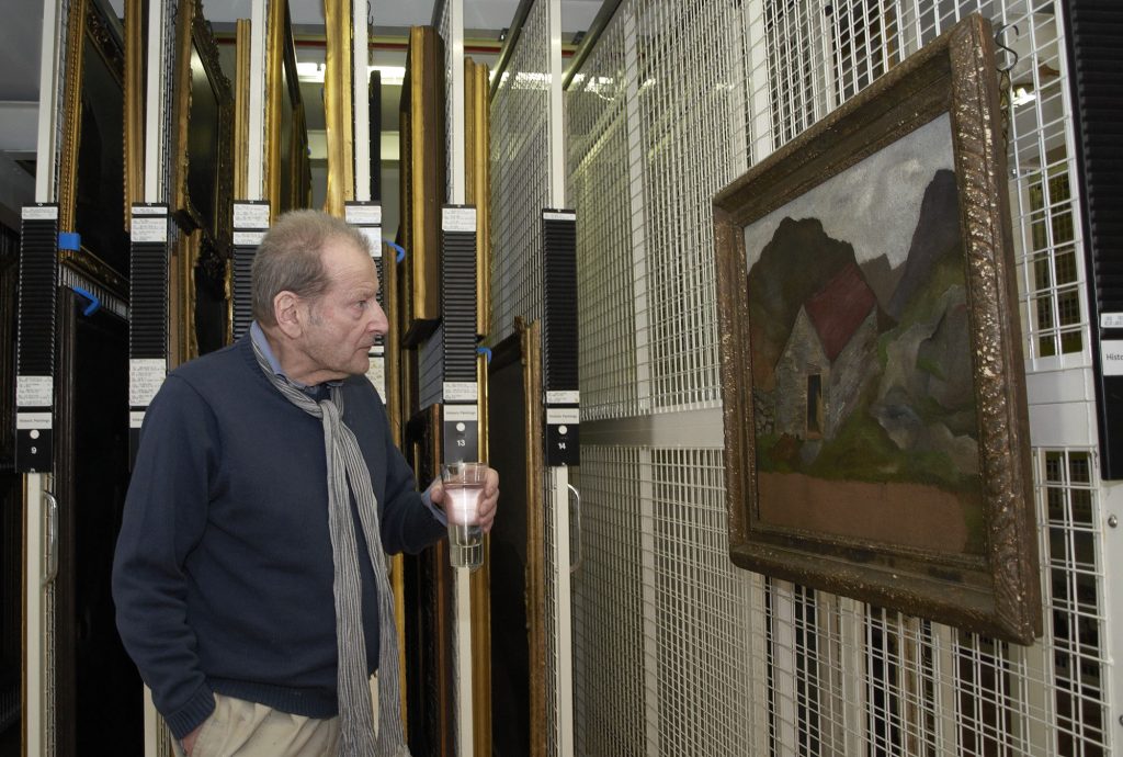 Lucian Freud visiting the Government Art Collection in 2011. He is holding a glass of water and looking at his painting in a store room.