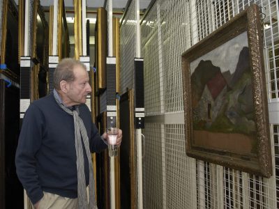 Lucien Freud visiting the Government Art Collection in 2011. He is holding a glass of water and looking at his painting in a store room.