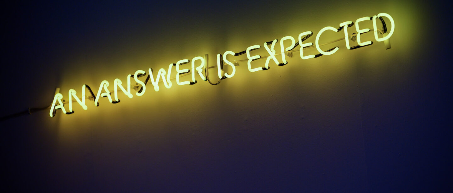 A yellow neon sign that says AN ANSWER IS EXPECTED