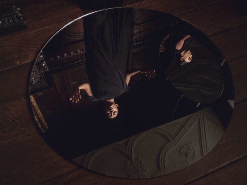 A work of art in the Foreign Commonwealth & Development Office; a woman wearing black stares at a rounded mirror on the floor.