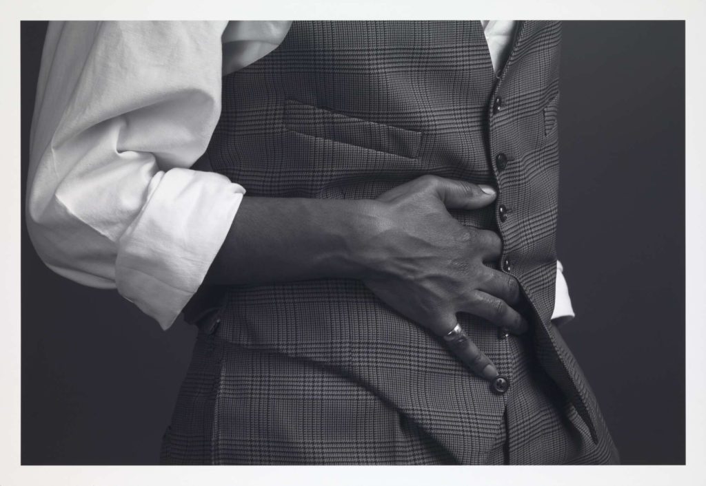 A black and white photo of a black man wearing a white shirt and a dark waistcoat; only the person's middle section can be seen.