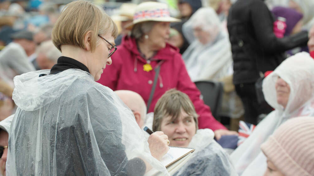 A woman in a raincoat is drawing in front of a crowd