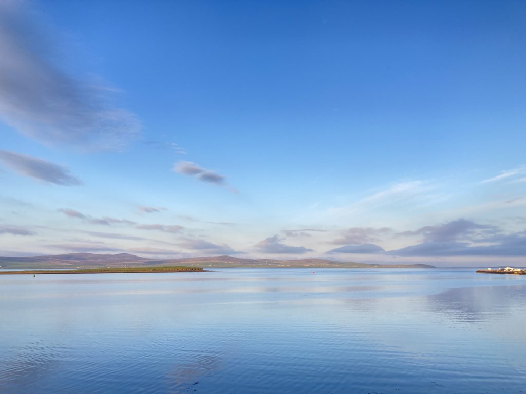 A photo of a bright blue sky with a few grey clouds, above an expanse of blue water