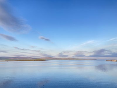 A photo of a bright blue sky with a few grey clouds, above an expanse of blue water