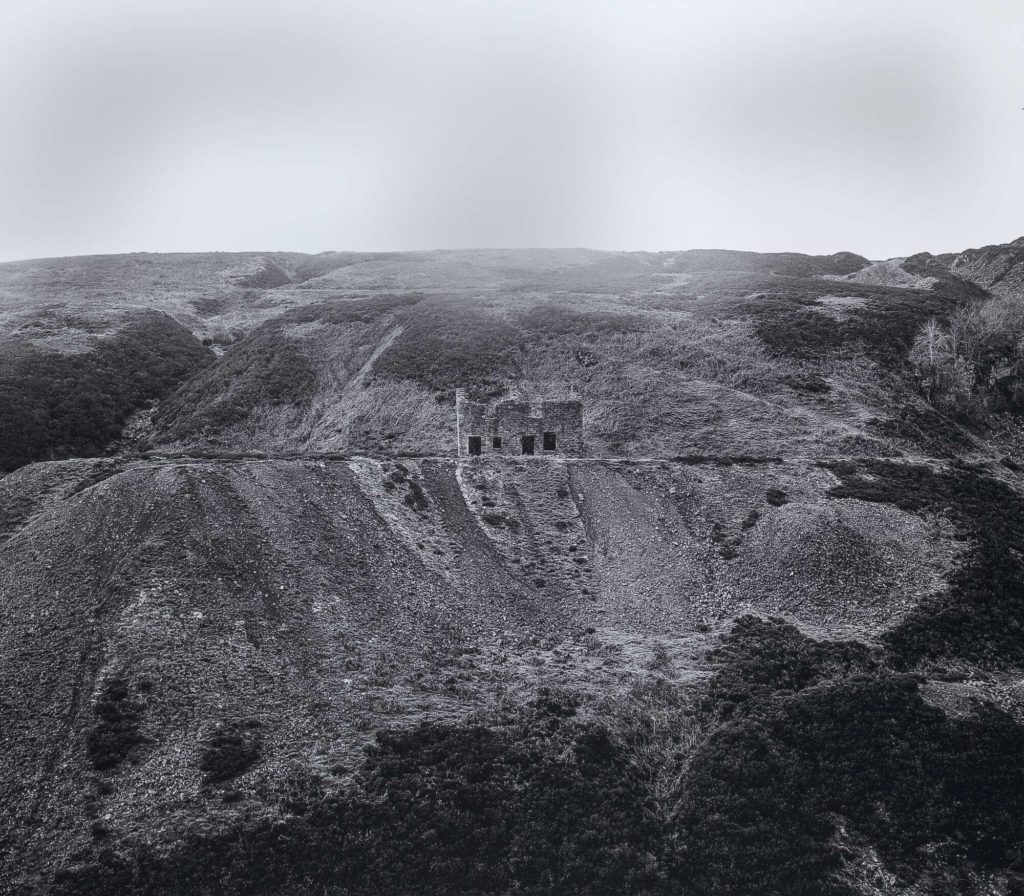 A black and white image of a rural landscape; in the centre is a small stone building.